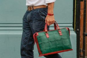 Man carrying a hand held stylish green and brown recycled leather bag from Elvis and Kresse